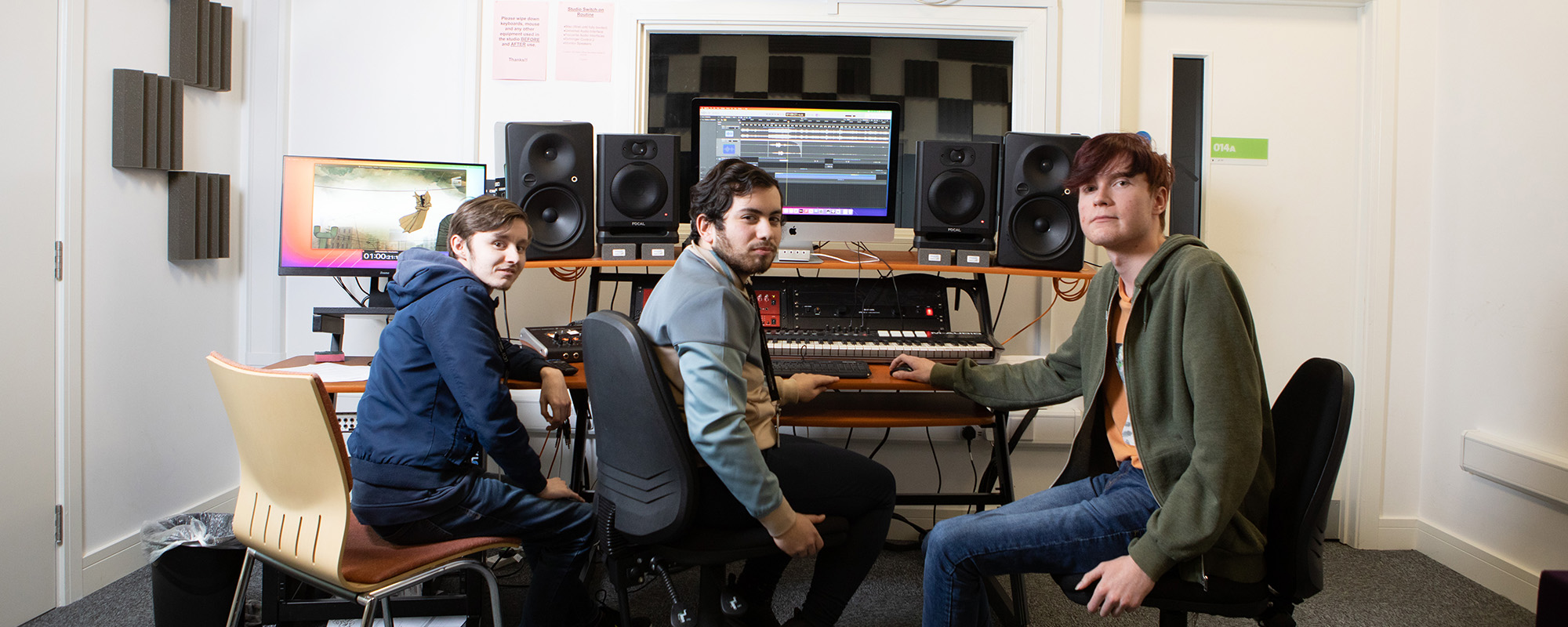 Three students sat around a mixing desk in a recording studio