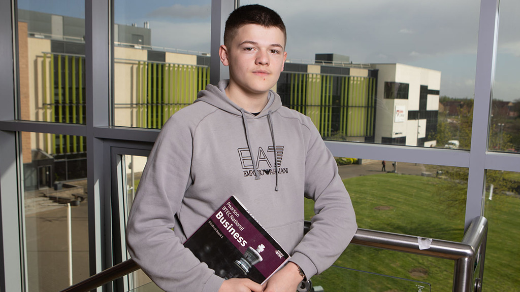 Male student standing holding a business book