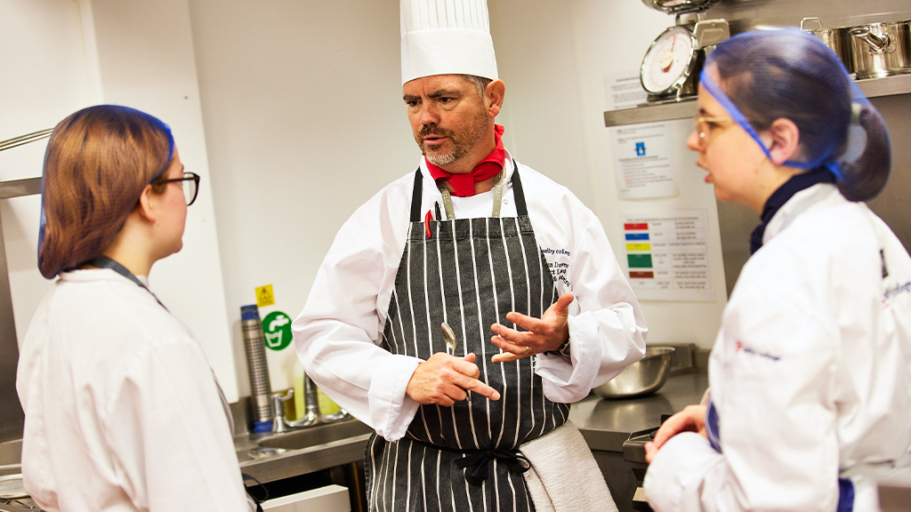 Catering staff teaching students in the kitchen