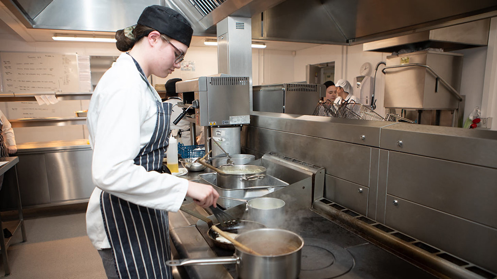 Student tending to a variety of dishes cooking on the hob